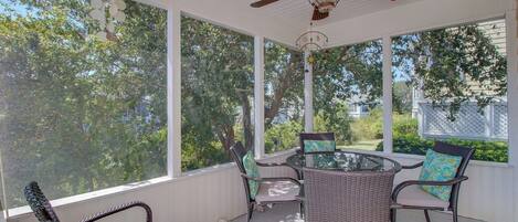 A covered patio with wicker furniture, a glass table, and a ceiling fan.