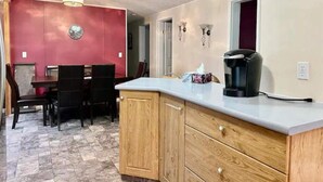 Una cocina con un mueble de madera, una cafetera y un comedor con sillas y una mesa.