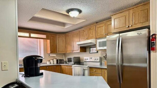 Una cocina con gabinetes de madera, un refrigerador de acero inoxidable, un microondas y una cafetera.
