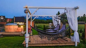 A hammock chair suspended over a wooden deck with a view of a mountain range in the background.