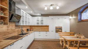 A modern kitchen with white cabinetry, wooden countertops, and a dining area with wooden tables and chairs.
