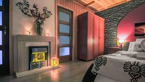 A bedroom with a fireplace, a bed with patterned bedding, a wardrobe, and a stone wall.