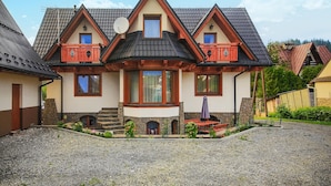 A two-story house with a stone foundation, a steeply pitched roof, and a small front porch with a stone bench.