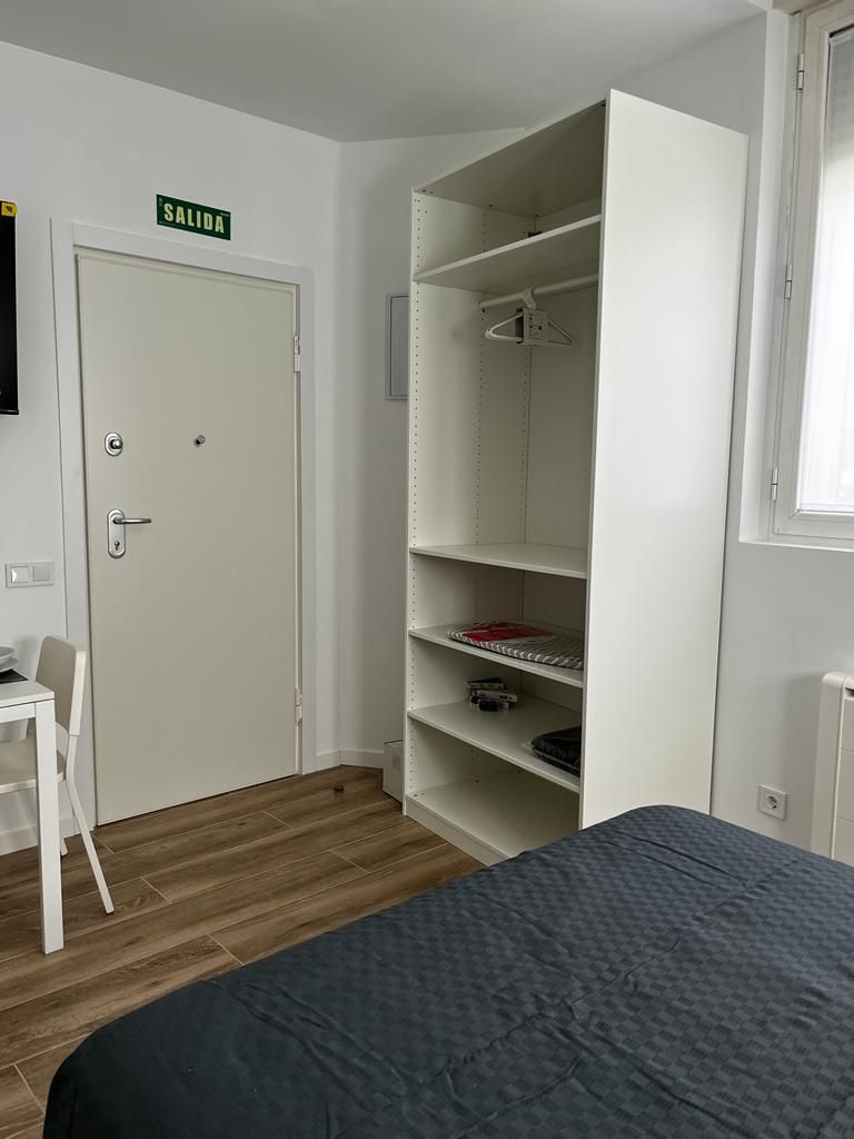 Quarto com uma cama, um guarda-roupa, uma escrivaninha e uma porta com a inscrição 'SALIDA'.