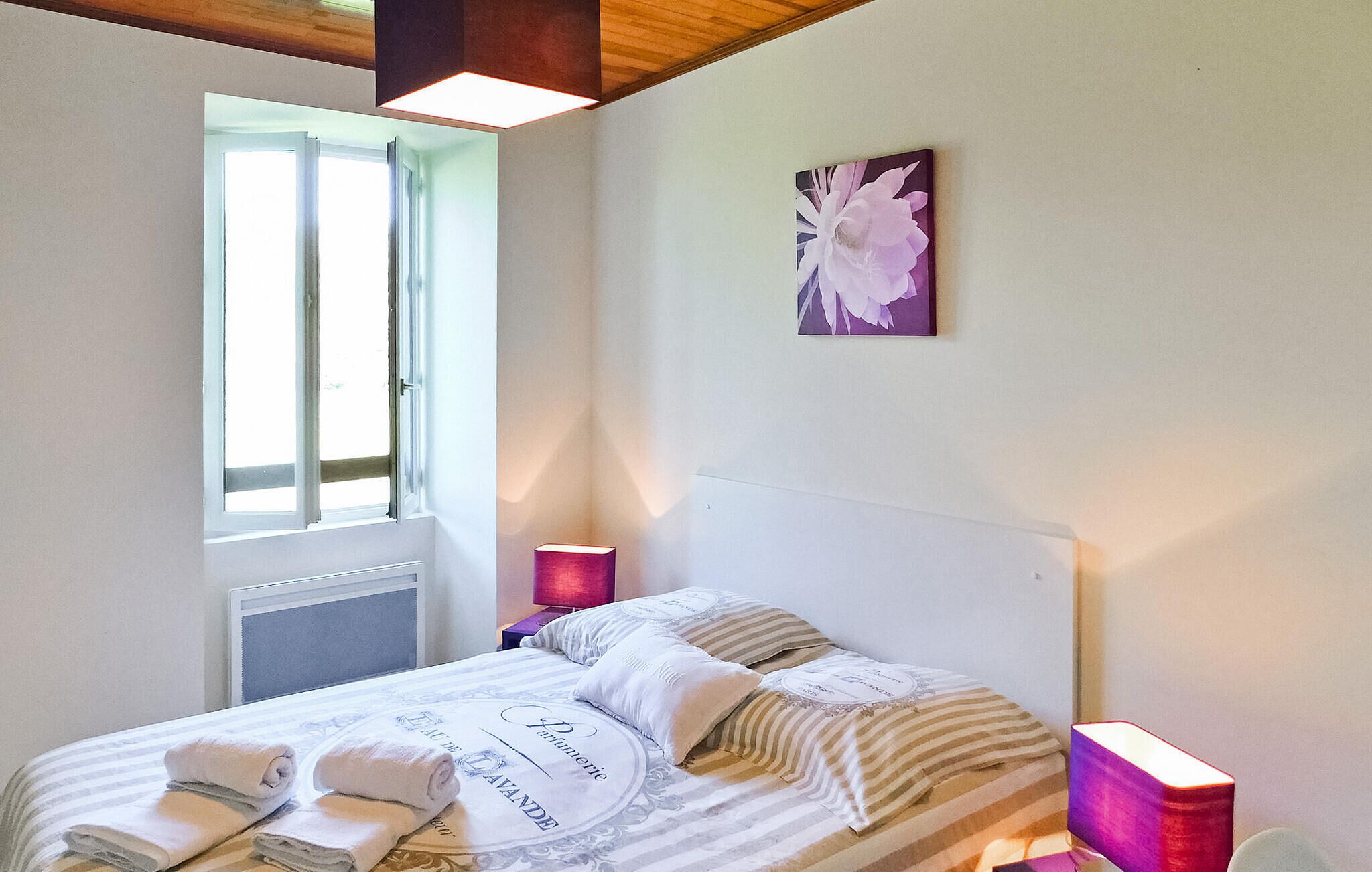 Une chambre à coucher avec un lit, une fenêtre, une lampe fixée au mur et une œuvre d’art à motifs floraux.