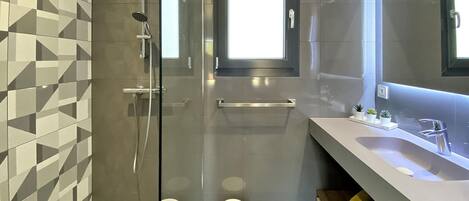 A modern bathroom with a glass-enclosed shower, a large mirror, and a vanity with a sink and towel rack.