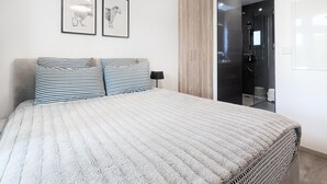 A neatly made bed with striped pillows, a framed picture of a leopard, and a modern bathroom with a glass shower enclosure.