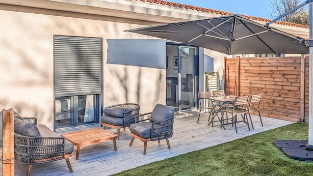 An outdoor patio with a table and chairs, a large umbrella, and a wooden fence.