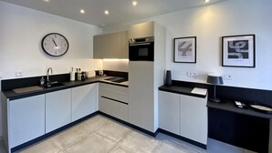 A modern kitchen with white cabinets, a black countertop, a built-in oven, a sink, and a clock on the wall.