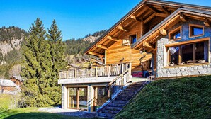 A wooden chalet with a stone facade, a wooden deck, and a staircase leading to the entrance.