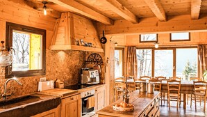 A rustic wooden cabin interior with a kitchen, dining area, and large windows.