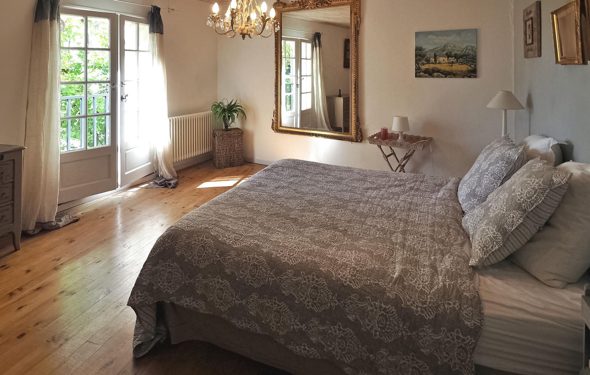 Un dormitorio con una cama grande, una araña, un espejo y un ventanal con cortinas.