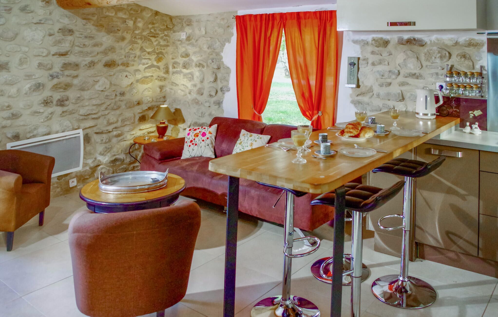 Ein gemütliches Wohnzimmer mit einer Steinwand, einem roten Sofa, einem Holzespeisetisch und einer Küchenzeile mit Herd und Schränken.