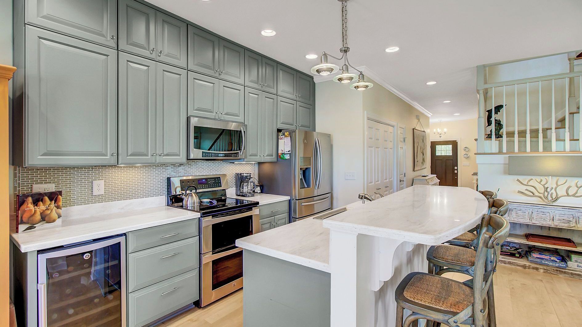 A modern kitchen with grey cabinets, stainless steel appliances, a large island with bar stools, and a chandelier.