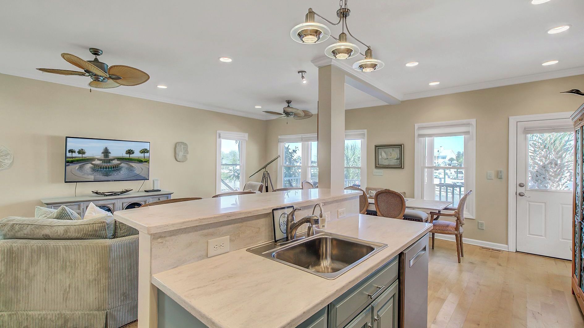 A kitchen with a central island, a dining area with chairs, a ceiling fan, recessed lighting, and a TV on the wall.