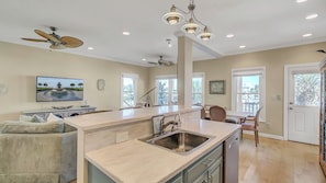 A kitchen with a central island, a dining area with chairs, a ceiling fan, recessed lighting, and a TV on the wall. - 26 Morgans Cove Drive by Avantstay Unique Marina Location (Isle of Palms)