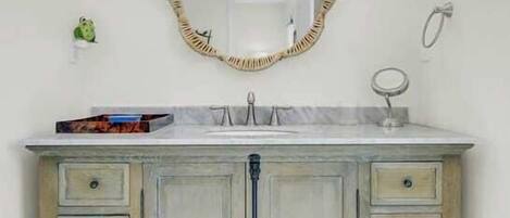 Un baño con tocador blanco, un espejo con marco decorativo, un sujetatowelas y un jabonera.