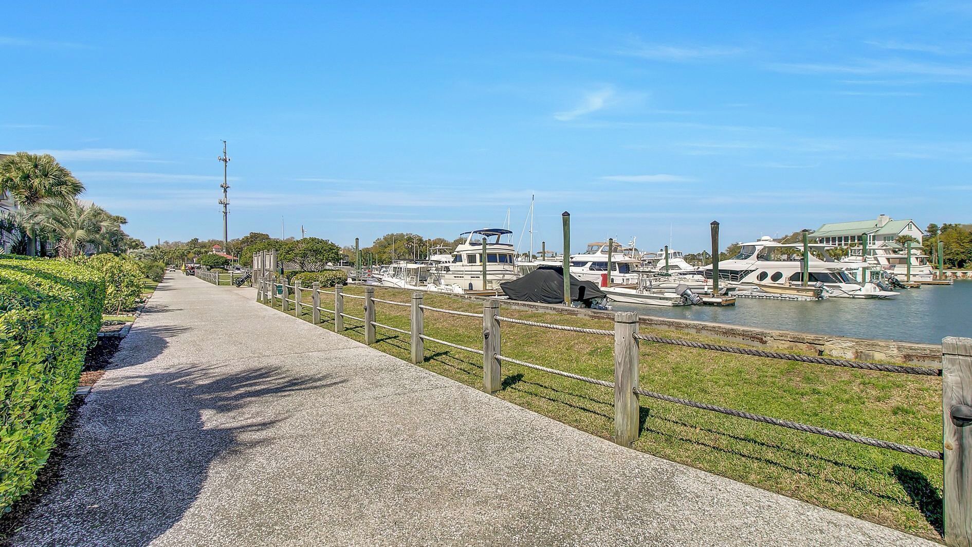 A marina with boats docked, a walking path alongside, and a clear sky.