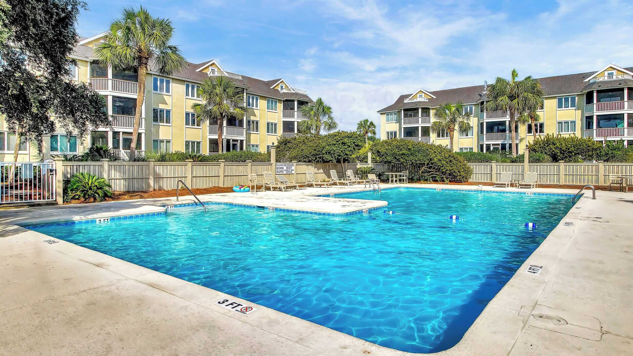 A rectangular pool with clear blue water, surrounded by a concrete deck and a wooden fence.