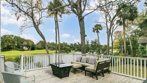 Eine Holzterrasse mit Gartenmöbeln, darunter ein Tisch und Stühle, mit Blick auf einen Golfplatz.