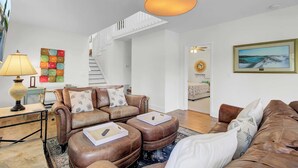 Ein modernes Wohnzimmer mit einem braunen Ledersofa, einem Couchtisch und einer Lampe. Eine Treppe führt in einen anderen Raum.