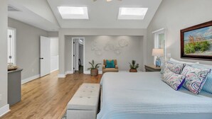 Ein geräumiges Schlafzimmer mit einem großen Bett, einem Deckenventilator, Dachfenstern und einem Landschaftsbild.