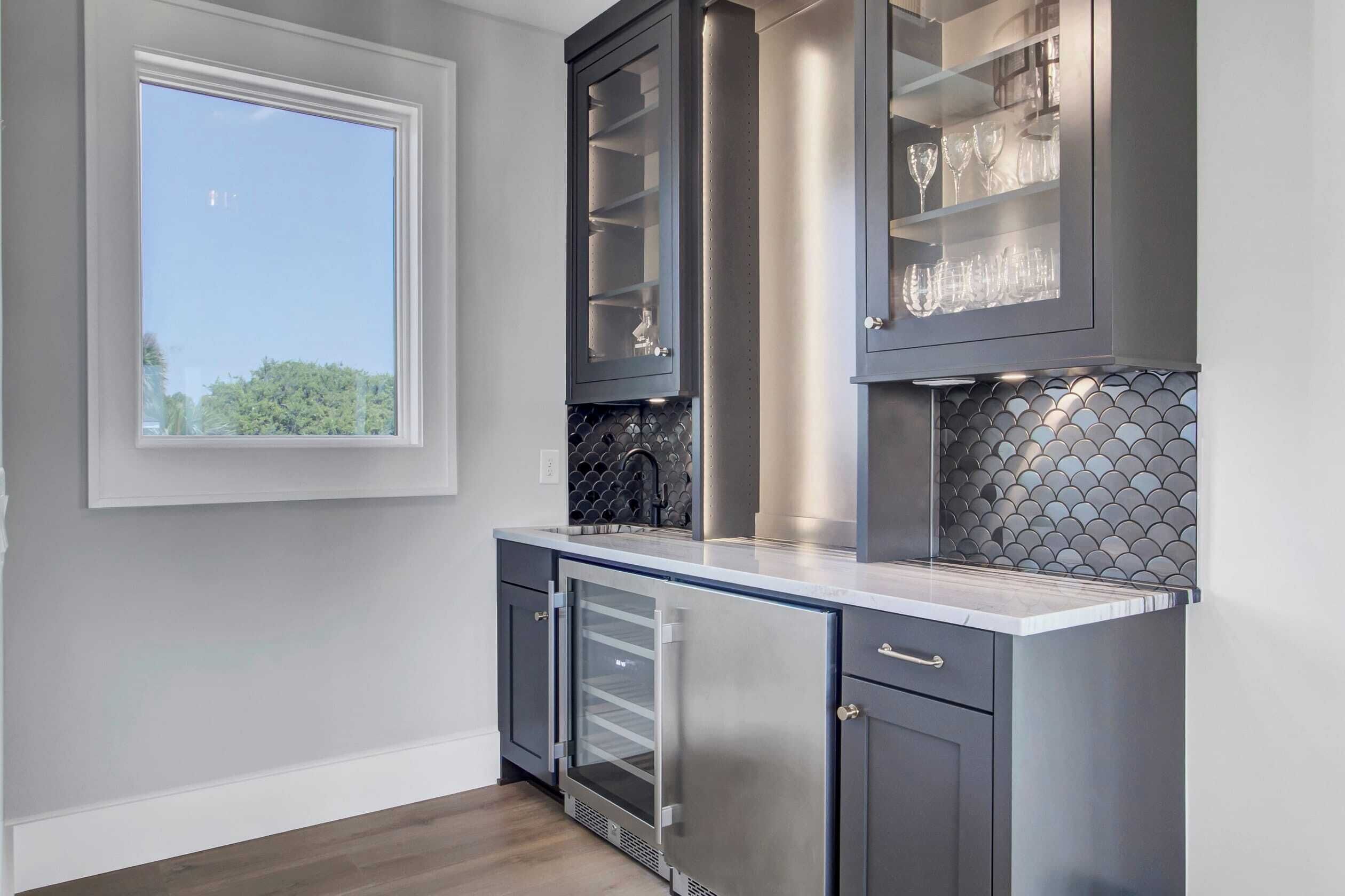 A modern kitchen with grey cabinetry, a built-in wine rack, and a window providing natural light.