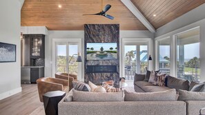 A modern living room with a large TV, comfortable seating, and a view of the outdoors. - 3 47th Avenue by Avantstay Oceanfront + Private Pool + View (Isle of Palms)