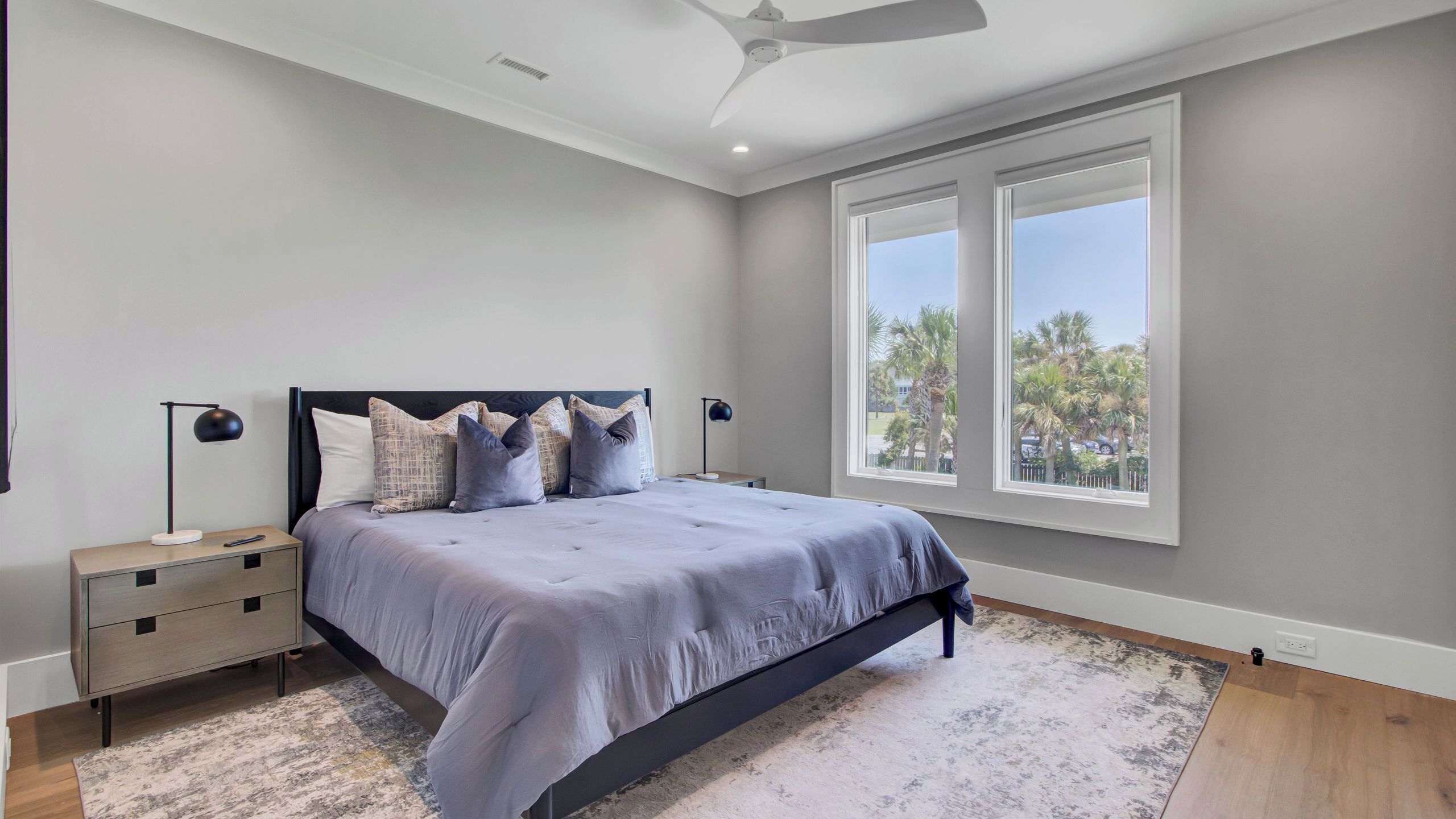 A bedroom with a bed, nightstands, a ceiling fan, and large windows.