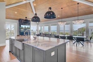 A spacious kitchen with a large island, modern pendant lights, and a view of the ocean. - 3 47th Avenue by Avantstay Oceanfront + Private Pool + View (Isle of Palms)
