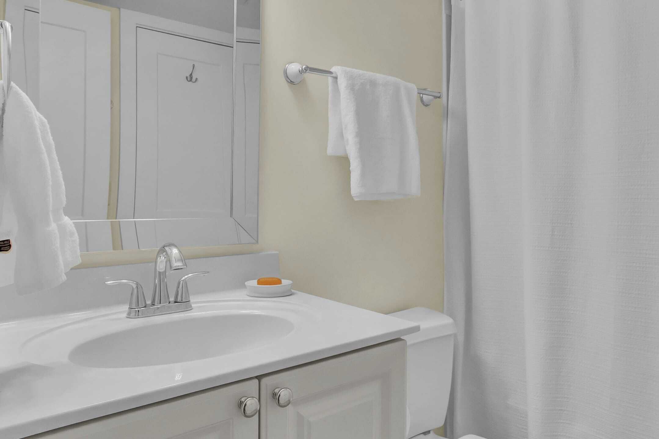 Une salle de bain avec un lavabo blanc, un miroir, un porte-serviettes et un rideau de douche.