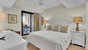 Une chambre d’hôtel équipée d’un lit, d’un bureau, d’une chaise, d’une table de chevet, d’une lampe et d’un ventilateur de plafond.