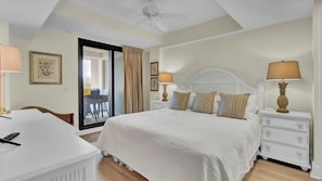 A hotel room with a bed, a desk, a chair, a nightstand, a lamp, and a ceiling fan. - 303a Shipwatch by Avantstay Ocean View, Shared Pool, Boardwalk to Beach (Isle of Palms)