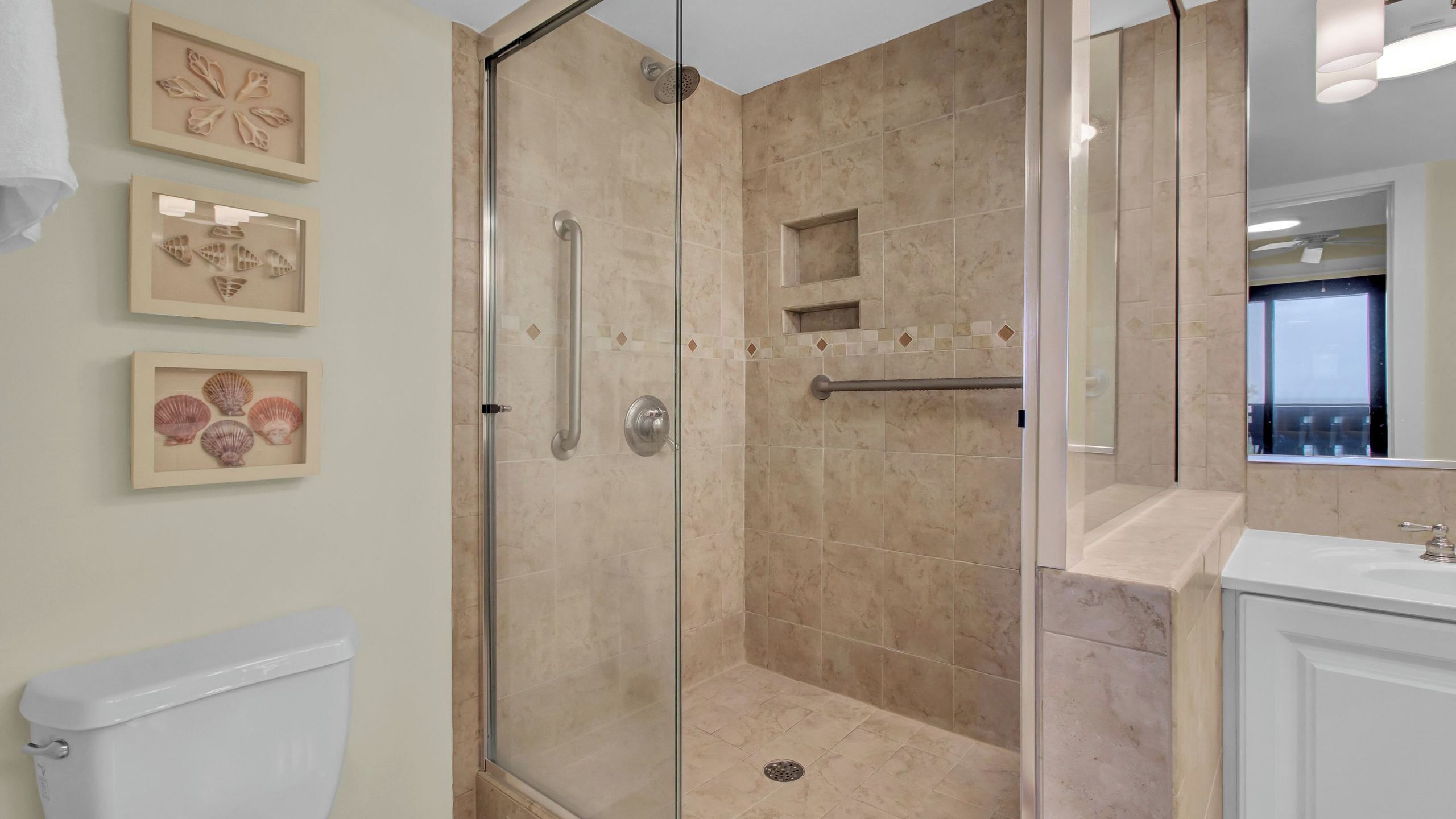 A modern bathroom with a glass-enclosed shower, a toilet, a sink, and framed artwork on the wall.