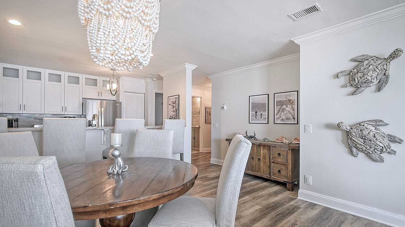Un coin repas avec une table ronde en bois, des chaises à revêtement blanc et un lustre.