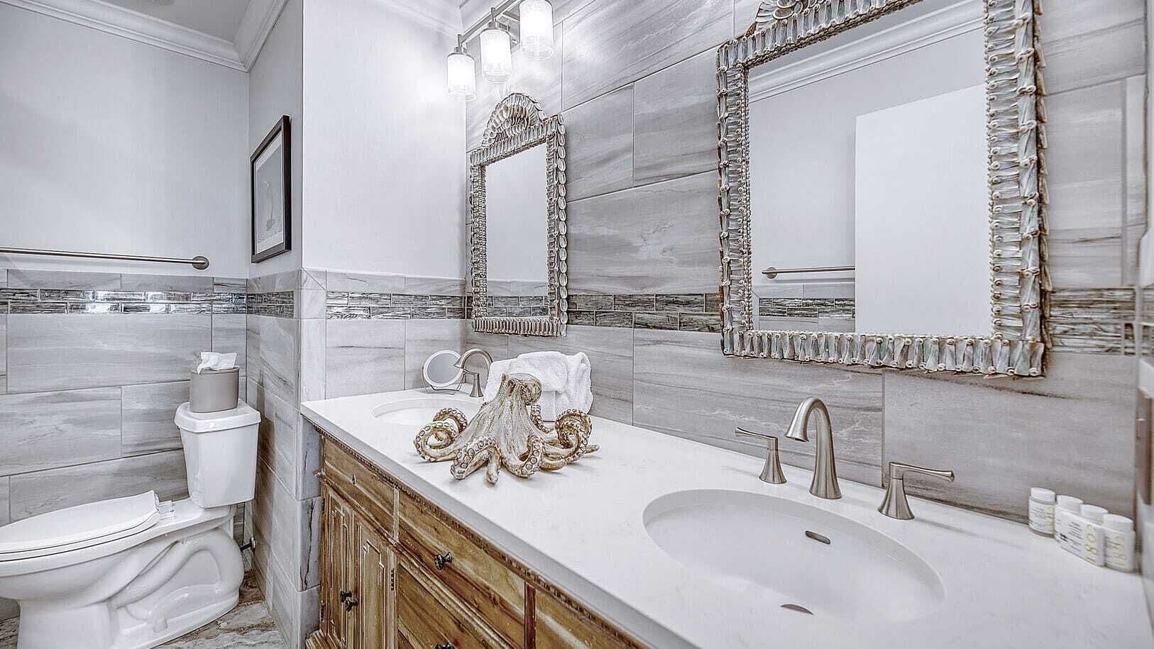 A modern bathroom with a marble vanity, two sinks, and a large mirror with decorative frames.