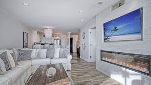 Un salon moderne avec un canapé blanc, une cheminée et un grand tableau représentant une scène de plage.