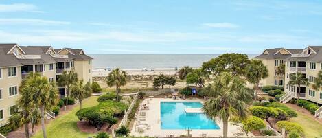 Hotel aan het strand met zwembad, palmbomen en uitzicht op de oceaan.