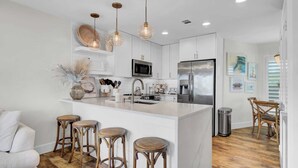 A modern kitchen with white cabinetry, a central island with stools, stainless steel appliances, and pendant lighting.