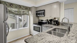 Una cocina moderna con encimera de granito, electrodomésticos de acero inoxidable y una ventana con cortina estampada.