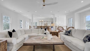 A spacious living room with a large sectional sofa, a wooden coffee table, and a dining area with a wooden table and chairs.