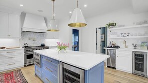 A modern kitchen with white cabinetry, stainless steel appliances, a central island, and pendant lighting. - 6 36th Avenue by Avantstay Stunning Private Pool (Isle of Palms)