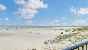 A beach with a clear sky, sandy dunes, and a wooden fence.