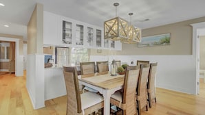 A modern kitchen with white cabinetry, a dining area with wicker chairs, and a hanging light fixture.