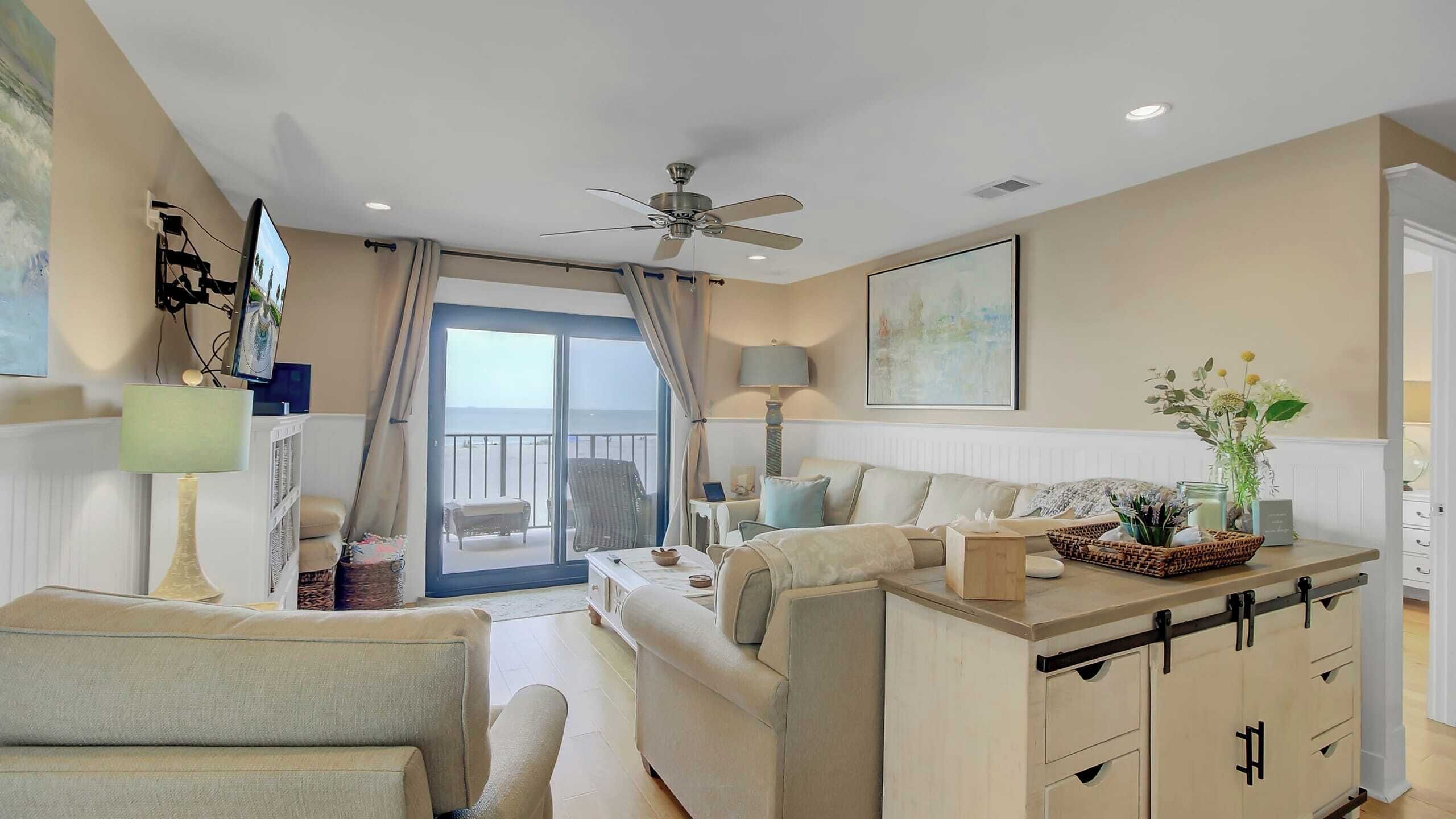 A spacious living room with a balcony, a ceiling fan, and a view of the sea.