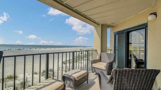A balcony with wicker furniture overlooking a beach.