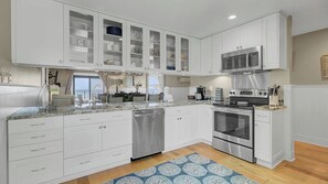 Una cocina moderna con armarios blancos, electrodomésticos de acero inoxidable y vistas al exterior.