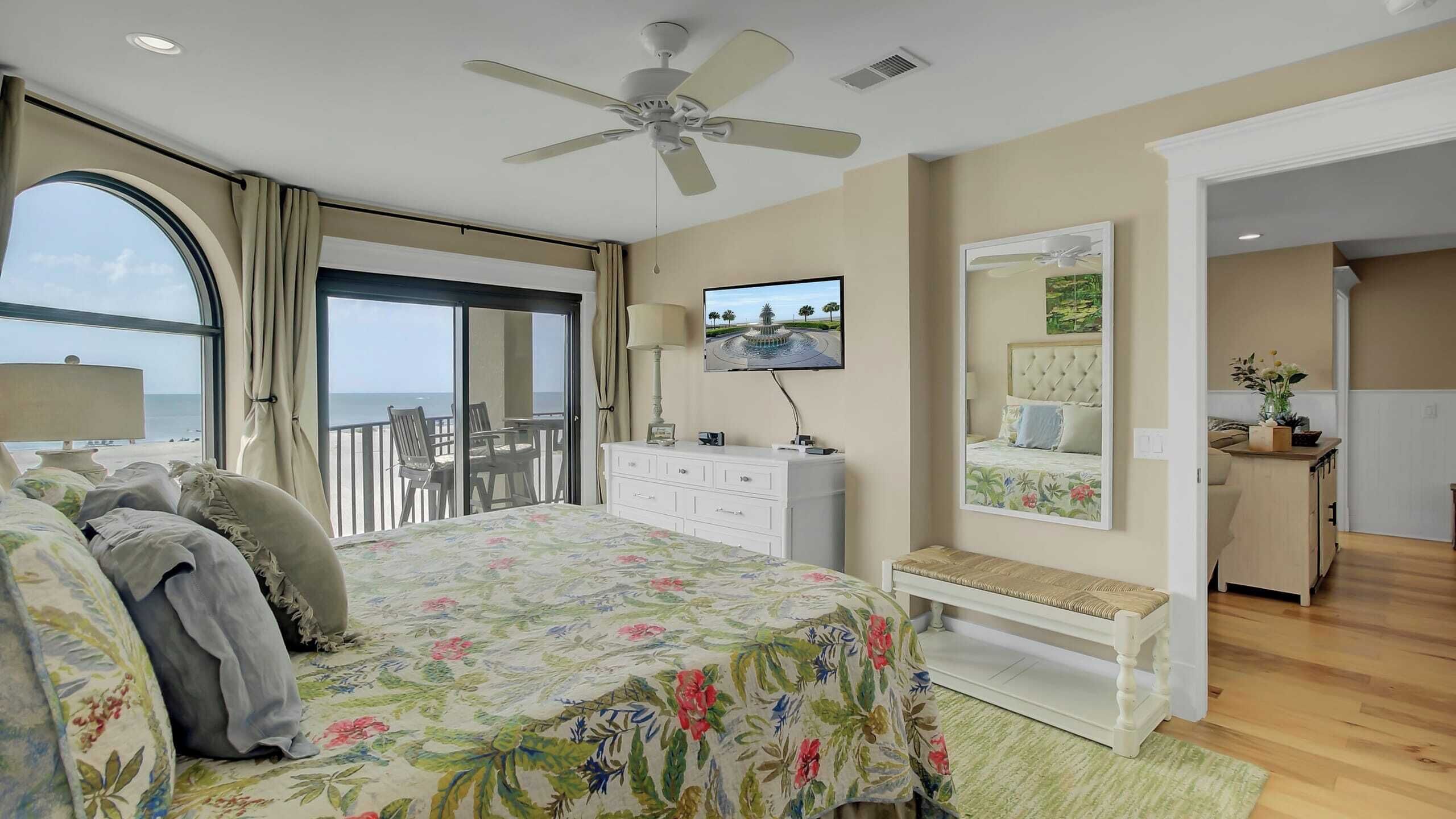 A bedroom with a bed, a dresser, a television, and a balcony with a view of the sea.