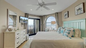 A bedroom with a bed, dresser, TV, and a view of the beach.