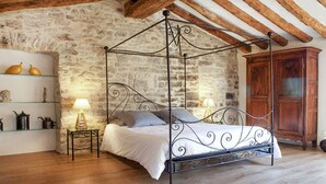 A four-poster bed with a metal frame, a stone wall, wooden beams, a wooden cabinet, and a small table with a lamp. - Gorgeous home in Carnas (Carnas)